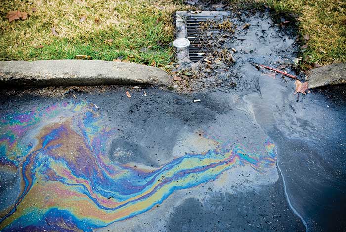 Oil contaminated stormwater runoff flowing into a partially clogged storm drain.